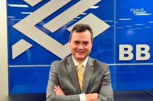 Homem sorridente de terno e gravata amarela, braços cruzados, em frente a logotipo do BB e investnews.