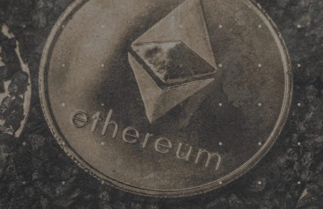 Close-up de moeda Ethereum metálica com seu logo e o nome em relevo, em fundo escuro granulado.