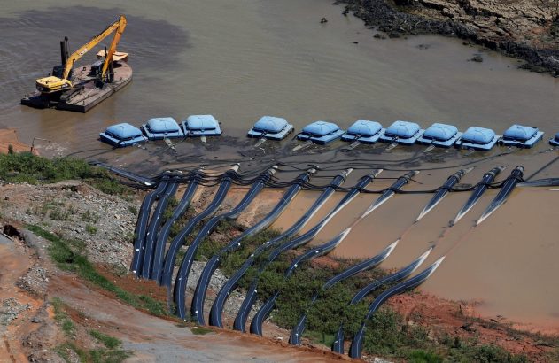 Equipamentos de dragagem e bombeamento: escavadeira em balsa, bombas e tubulações em água barrenta.