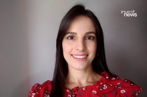 Mulher de cabelo escuro sorrindo, vestindo blusa vermelha floral. No canto superior direito, o logo "invest news".