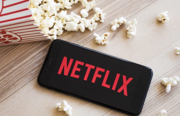 Pipoca derrubada ao lado de um celular com a logo da Netflix na tela, ilustrando o tema: história da netflix