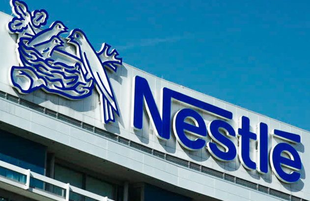 Edifício Nestlé com seu logo azul: um ninho com pássaros. Visível sob céu azul claro.