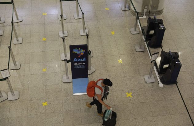 Passageiro com bagagem na área de check-in da Azul, com marcas de distanciamento no chão do aeroporto.