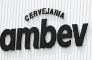 Letreiro preto 'CERVEJARIA ambev' em relevo numa parede branca corrugada.