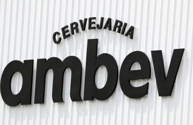 Letreiro preto 'CERVEJARIA ambev' em relevo numa parede branca corrugada.