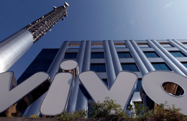 Vista de baixo para cima: Letreiro Vivo, prédio moderno e torre de telecomunicações sob céu azul.
