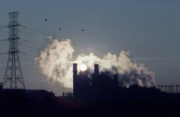 Usina de energia e torre de transmissão em silhueta contra o sol e vapor no céu.