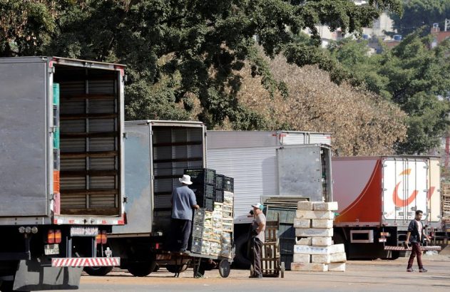Pessoas movimentam caixas e mercadorias de caminhões de entrega com portas abertas em área de carga.