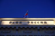 Letreiro 'Banco da Rússia' iluminado em prédio, bandeira russa e céu azul-escuro.