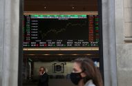 Tela de bolsa de valores com dados e gráfico do IBOVESPA, vista através de entrada com pessoas mascaradas.