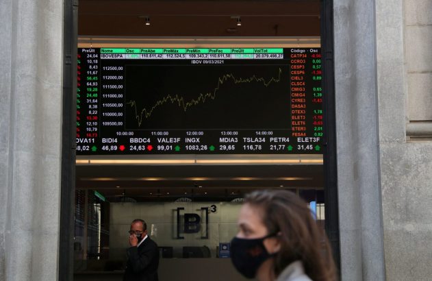 Tela de bolsa de valores com dados e gráfico do IBOVESPA, vista através de entrada com pessoas mascaradas.