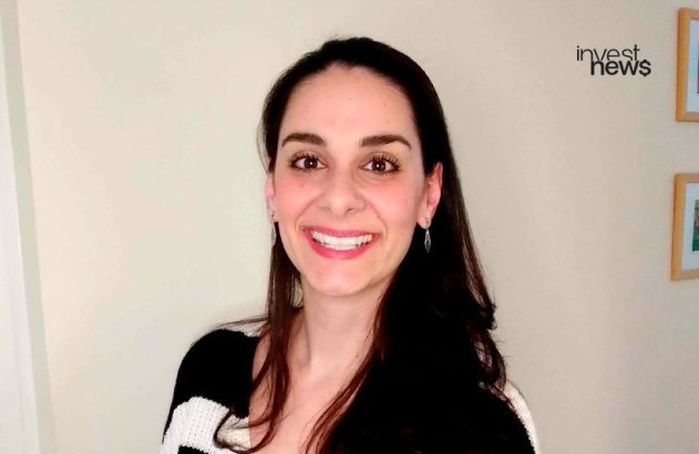 Mulher sorridente, cabelo escuro e suéter listrado. Fundo claro com logo "invest news" no canto superior direito.