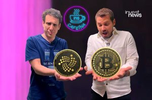 Dois homens seguram criptomoedas Bitcoin e IOTA; um surpreso, outro cético. Logo InvestNews ao fundo.