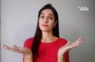 Mulher de camisa vermelha encolhe os ombros com expressão de incerteza e mãos abertas.