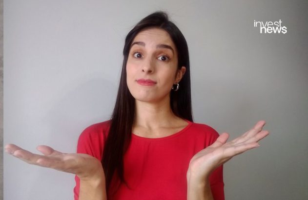 Mulher de camisa vermelha encolhe os ombros com expressão de incerteza e mãos abertas.