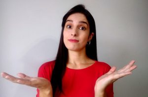 Mulher de camisa vermelha, expressão confusa, mãos abertas em gesto de "não sei".