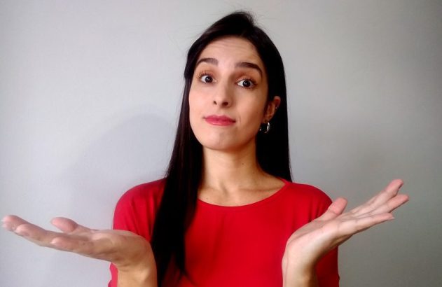 Mulher de camisa vermelha, expressão confusa, mãos abertas em gesto de "não sei".