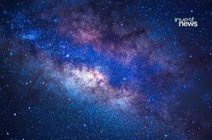 Via Láctea no céu noturno, repleta de estrelas e cores vibrantes. Marca d'água 'invest news'.