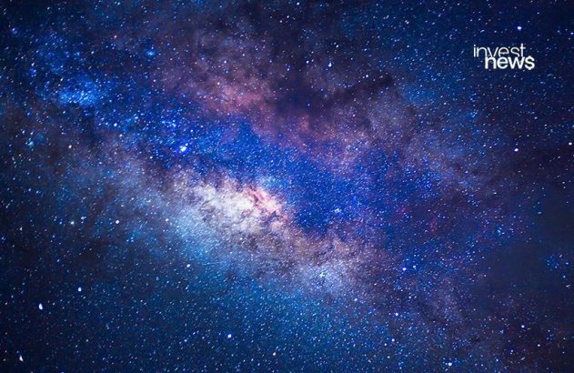 Via Láctea no céu noturno, repleta de estrelas e cores vibrantes. Marca d'água 'invest news'.