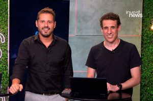 Dois homens sorrindo para a câmera em estúdio, com laptop em uma mesa e logo 'invest news' visível.