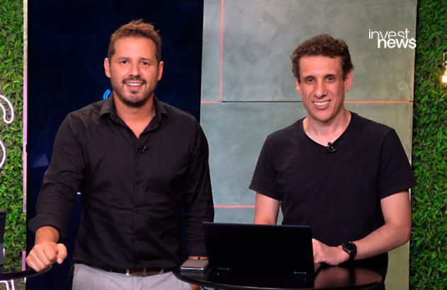 Dois homens sorrindo para a câmera em estúdio, com laptop em uma mesa e logo 'invest news' visível.