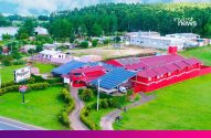 Aéreo: Motel Pepper vermelho com telhados cheios de painéis solares, cercado por paisagem verde.