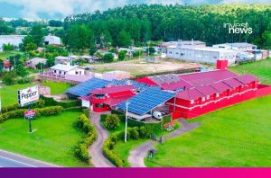 Aéreo: Motel Pepper vermelho com telhados cheios de painéis solares, cercado por paisagem verde.