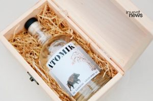 Garrafa de Atomik Grain Spirit com javali no rótulo em caixa de madeira com palha, aberta.