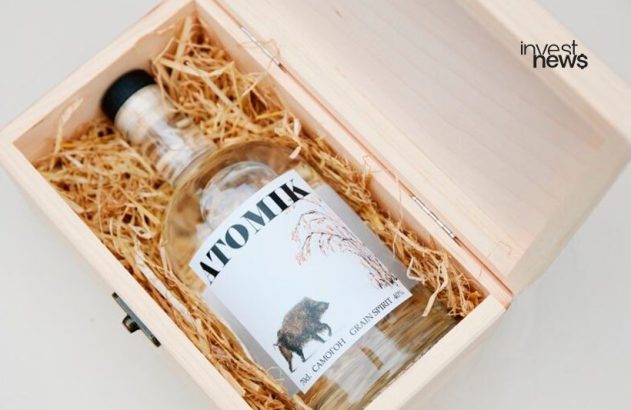 Garrafa de Atomik Grain Spirit com javali no rótulo em caixa de madeira com palha, aberta.