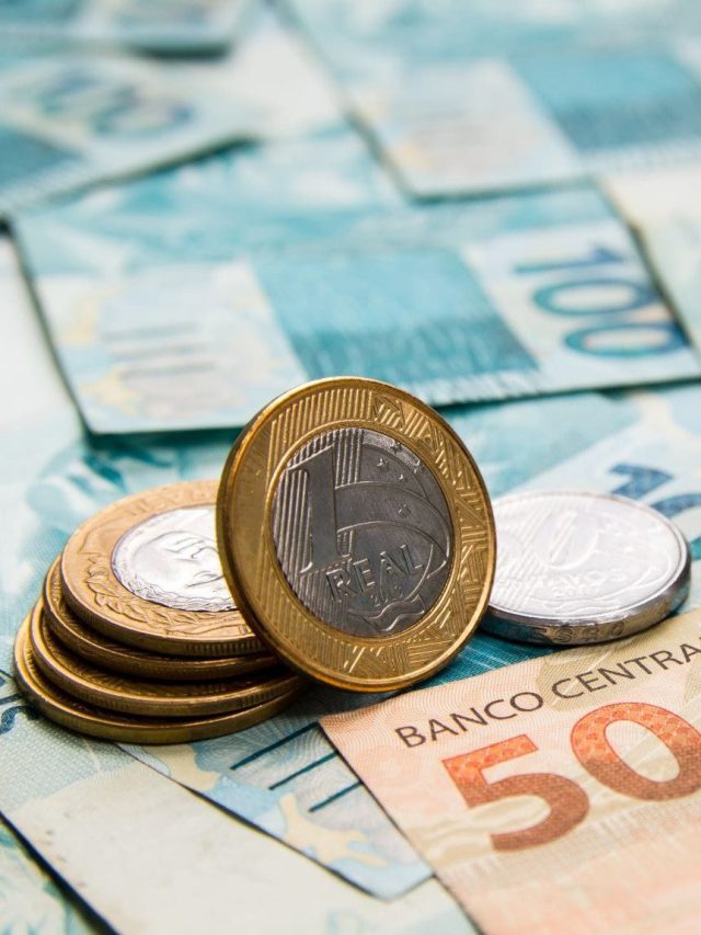 Moedas de Real e cédulas brasileiras. Uma moeda de 1 Real em pé sobre notas de 50 e 100 Reais.