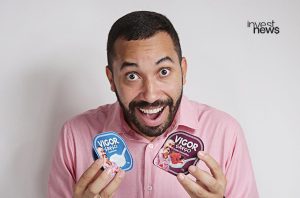 Homem sorridente e de olhos arregalados segura dois potes de iogurte "Vigor Grego" com sua própria foto.