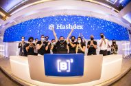 Grupo de pessoas com máscaras celebra lançamento da Hashdex na B3. Telão azul com logo e pontos brancos ao fundo.
