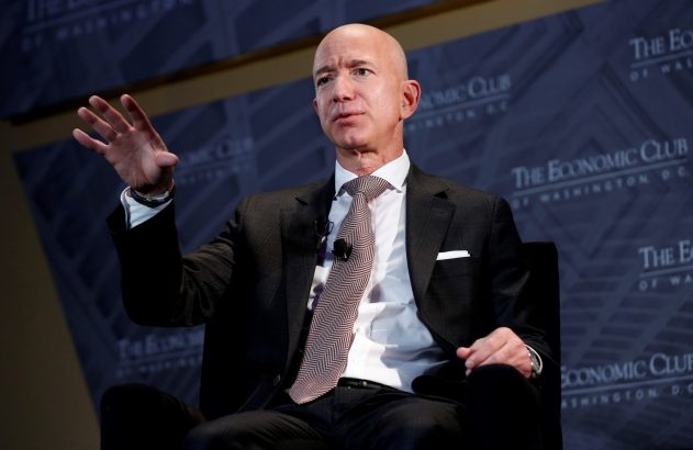 Dono da Amazon, Jeff Bezos, de terno, fala e gesticula sentado em evento do Economic Club.