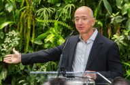 Jeff Bezos discursa e gesticula em pódio. Ao fundo, parede de plantas.