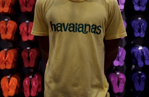 Pessoa em camiseta amarela Havaianas, com chinelos coloridos da marca expostos ao fundo.