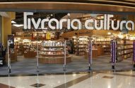 Livraria Cultura: entrada de vidro mostra amplo interior com estantes cheias de livros. Monitores e banners na frente.