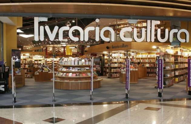 Livraria Cultura: entrada de vidro mostra amplo interior com estantes cheias de livros. Monitores e banners na frente.
