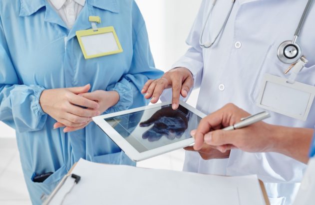 Três profissionais de saúde analisam imagem médica em tablet e fazem anotações.