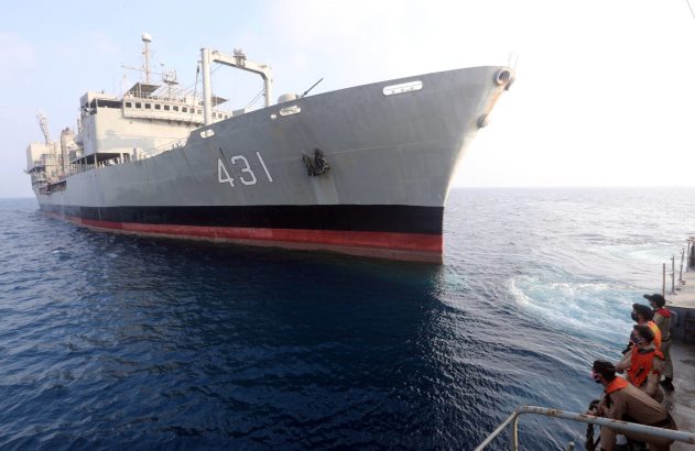 Navio cinza '431' em alto mar. Tripulantes com coletes observam de outra embarcação.