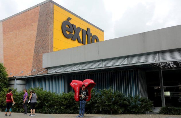Homem com adereço promocional vermelho da 'Une' ('melhor juntos') em frente ao letreiro 'Éxito'.