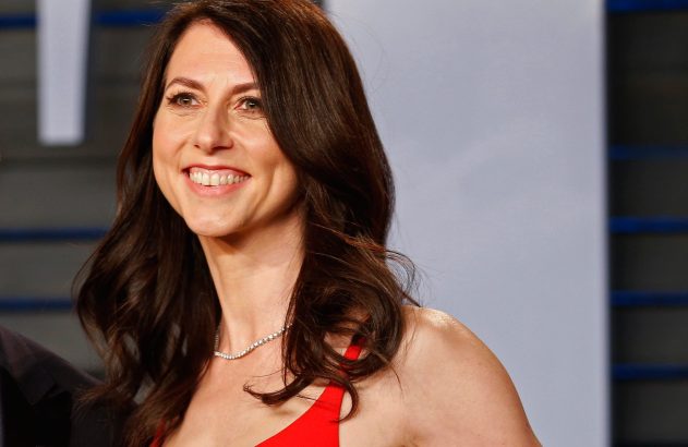 Mulher sorrindo com cabelos castanhos, vestindo um vestido vermelho e um colar de diamantes. Olhando para cima.