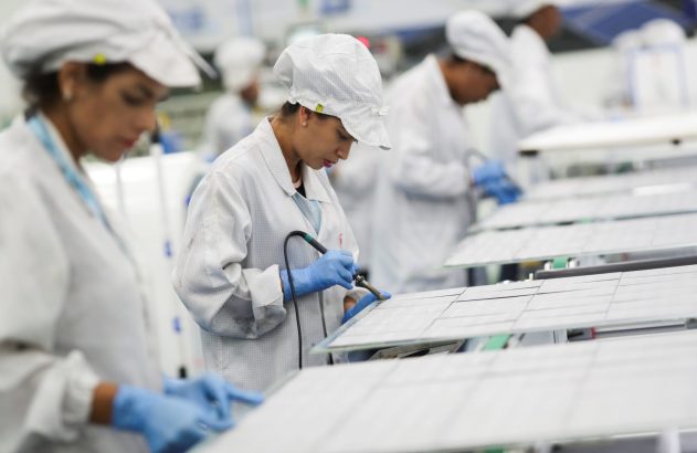 Operária em jaleco soldando painéis em linha de montagem de fábrica.