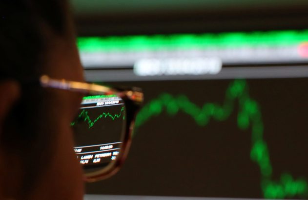 Pessoa de óculos observa gráfico financeiro verde em tela de computador, com reflexo visível nas lentes.