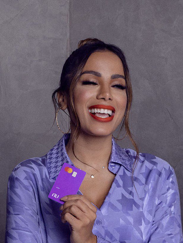 Mulher sorridente com olhos fechados, segurando um cartão roxo Nubank.