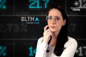 Mulher com óculos, expressão de dúvida, diante de tela digital exibindo dados do mercado financeiro e logos "investnews".