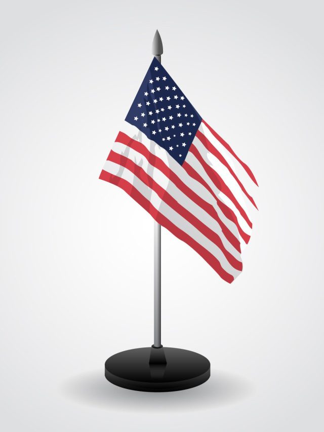 Bandeira dos Estados Unidos de mesa, erguida em mastro com base, contra um fundo claro e liso.