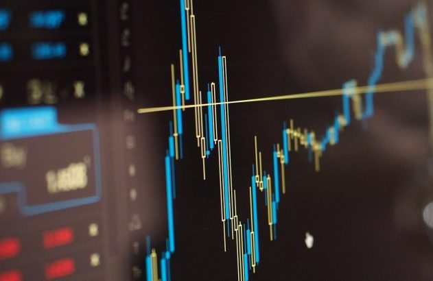 Gráfico Forex com candlesticks azuis e dourados em tela de computador de trading.