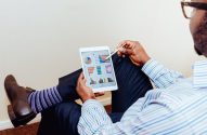 Homem de costas usa tablet com caneta para analisar gráficos e dados.