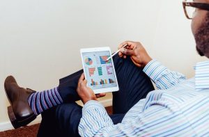 Homem de costas usa tablet com caneta para analisar gráficos e dados.