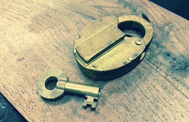 Cadeado e chave de latão antigos em superfície de madeira.